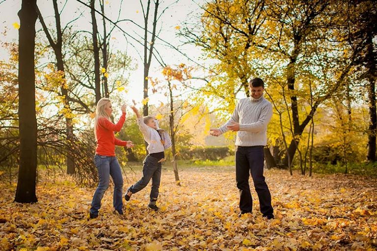 Family of three playing in autumn sunshine throwing leaves